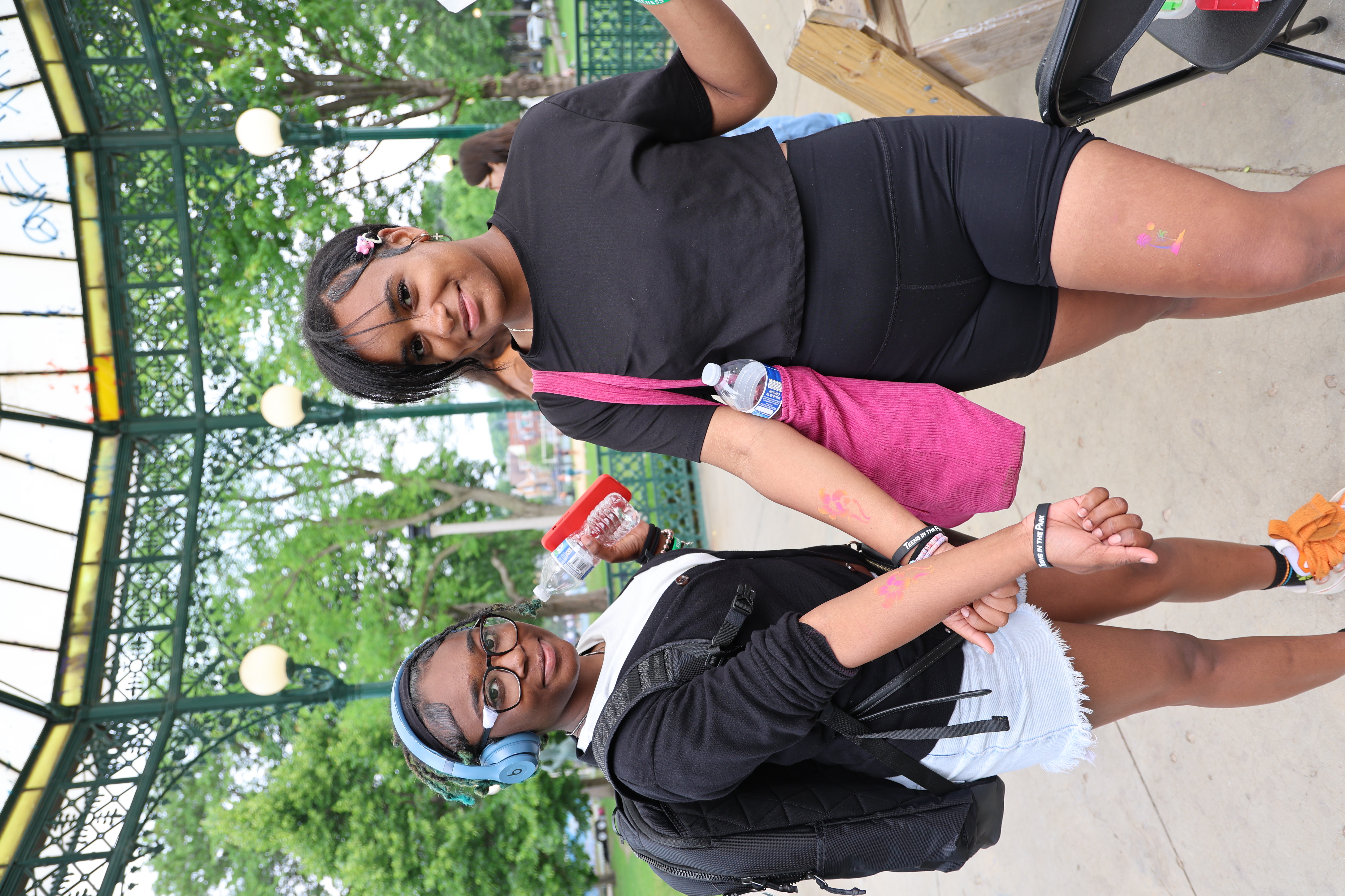 Two friends smile under a gazebo in a park.